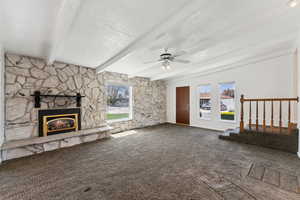 Unfurnished living room featuring ceiling fan, a textured ceiling, a fireplace, beamed ceiling, and carpet flooring