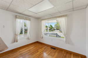 Empty room featuring baseboards, visible vents, light wood-type flooring, and a paneled ceiling