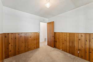 Carpeted empty room with visible vents, wainscoting, wooden walls, wallpapered walls, and a textured ceiling