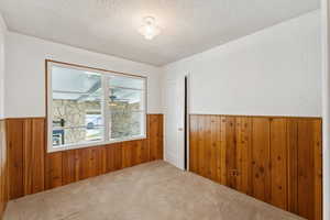 Unfurnished room featuring a textured ceiling, wood walls, and a wainscoted wall