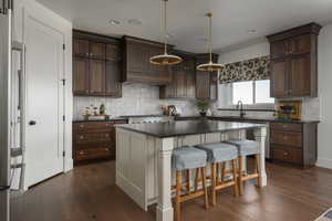 Kitchen with dark countertops, dark wood finished floors, a sink, premium range hood, and high end fridge