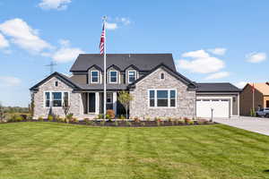 View of front of property featuring a front yard, concrete driveway, an attached garage, a shingled roof, and stone siding