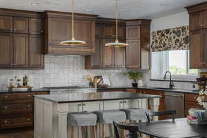 Kitchen with stainless steel dishwasher, dark countertops, a sink, backsplash, and hanging light fixtures