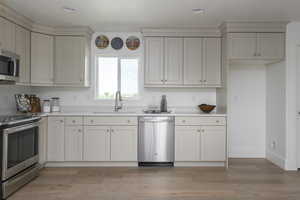 Kitchen featuring baseboards, light wood-type flooring, light countertops, a sink, and stainless steel appliances