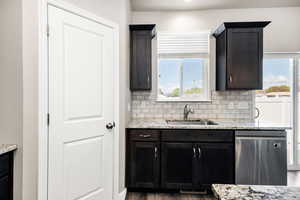 Kitchen with light stone countertops, a sink, dishwasher, wood finished floors, and tasteful backsplash