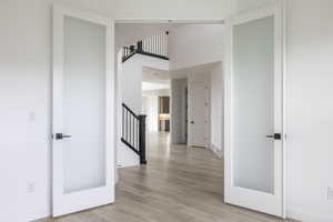 Corridor featuring stairway, baseboards, a high ceiling, and light wood-type flooring
