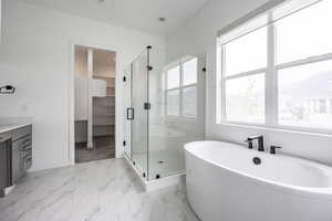 Full bathroom featuring marble finish floor, baseboards, a spacious closet, a soaking tub, and a stall shower
