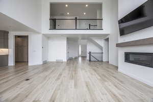Unfurnished living room featuring visible vents, light wood finished floors, a glass covered fireplace, and a high ceiling