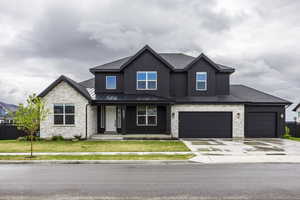 View of front of house with a front lawn, stone siding, a standing seam roof, a porch, and driveway