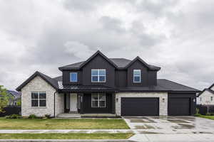 View of front of house with stone siding, a front yard, a standing seam roof, concrete driveway, and a porch
