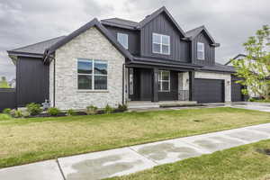 Craftsman-style house with covered porch, a front yard, stone siding, board and batten siding, and concrete driveway