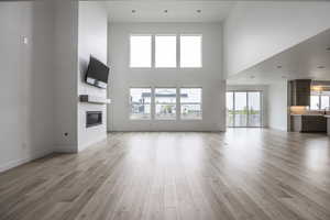 Unfurnished living room with a towering ceiling, a glass covered fireplace, baseboards, a sink, and light wood finished floors