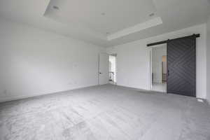 Unfurnished bedroom with baseboards, a barn door, a tray ceiling, and carpet flooring