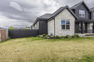 View of property exterior with board and batten siding, a lawn, and stone siding