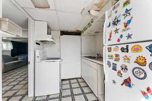 Kitchen with freestanding refrigerator, washer / dryer, range with electric stovetop, light floors, and a sink
