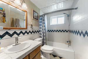 Full bathroom with tile walls, tile patterned floors, vanity, toilet, and shower / bath combo with shower curtain
