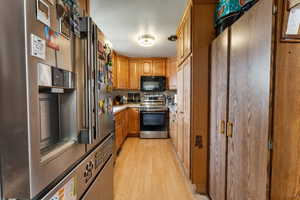 Kitchen with decorative backsplash, brown cabinetry, light countertops, stainless steel appliances, and light wood-style flooring
