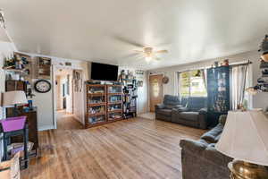 Living room with crown molding, baseboards, ceiling fan, and light wood finished floors