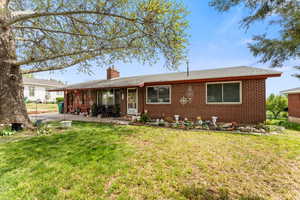 View of front of home featuring brick siding, a patio area, a front yard, and a chimney