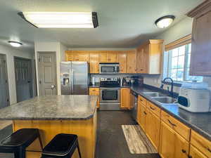 Kitchen featuring a sink, a textured ceiling, appliances with stainless steel finishes, and dark countertops