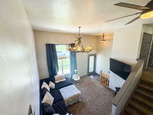 Living room featuring carpet floors, ceiling fan with notable chandelier, and a textured ceiling