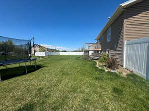 View of yard featuring fence, a trampoline, and a deck
