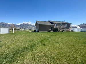 Back of house featuring a lawn, a deck with mountain view, fence, and stairs