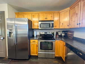 Kitchen featuring stone finish flooring, a textured ceiling, appliances with stainless steel finishes, and dark countertops