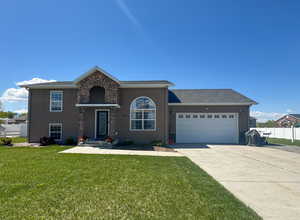 View of front of property featuring an attached garage, a front lawn, fence, and concrete driveway