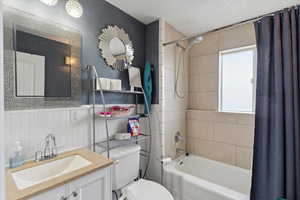 Full bath with vanity, wainscoting, shower / bathtub combination with curtain, and toilet