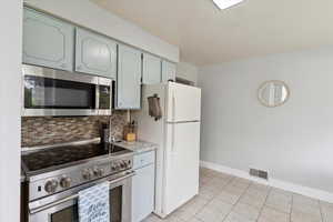 Kitchen with light countertops, appliances with stainless steel finishes, baseboards, decorative backsplash, and visible vents