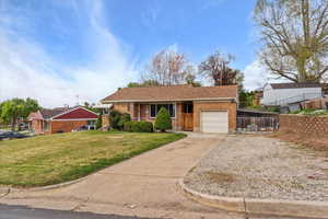 Ranch-style home with a front lawn, fence, brick siding, an attached garage, and driveway