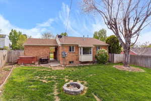 Back of house with a hot tub, brick siding, a yard, and a fenced backyard