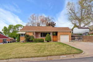 Ranch-style home featuring a garage, a front lawn, fence, brick siding, and concrete driveway
