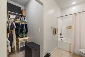 Bathroom with a walk in closet, tile patterned flooring, baseboards, toilet, and shower / tub combo with curtain