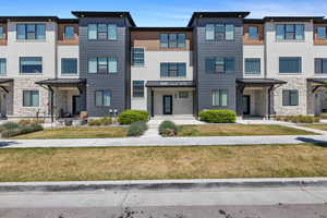 Townhome / multi-family property featuring a front yard, metal roof, stone siding, and a standing seam roof