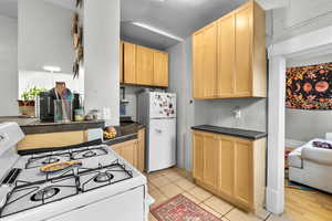 Kitchen featuring white appliances, dark countertops, light tile patterned floors, and light brown cabinets