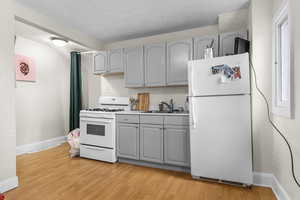 Kitchen with a sink, light wood finished floors, gray cabinetry, and white appliances