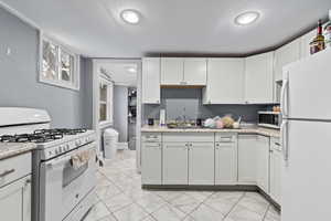 Kitchen featuring a sink, light stone countertops, white appliances, and white cabinetry