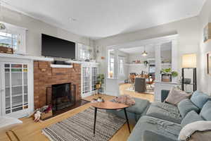 Living room featuring a brick fireplace, decorative columns, and wood finished floors