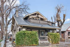 Bungalow-style house featuring a porch, a chimney, fence, a balcony, and a shingled roof