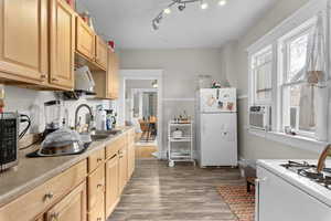 Kitchen featuring dark wood-style flooring, a sink, light countertops, light brown cabinets, and white appliances