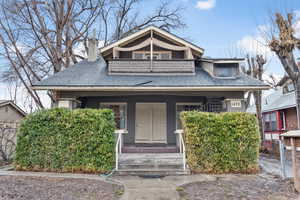 Bungalow-style home with a shingled roof, covered porch, a chimney, and a balcony