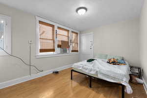 Bedroom with a textured ceiling, baseboards, multiple windows, and wood finished floors
