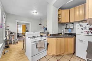 Kitchen featuring open shelves, a sink, a peninsula, light brown cabinets, and white appliances