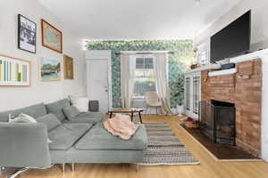 Living area with a brick fireplace, wallpapered walls, and wood finished floors