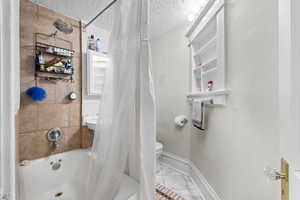 Bathroom featuring baseboards, marble finish floor, a textured ceiling, and toilet