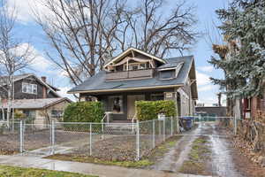 Bungalow-style house with a shingled roof, a fenced front yard, a gate, covered porch, and driveway