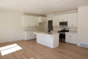 Kitchen featuring a kitchen island with sink, visible vents, appliances with stainless steel finishes, a sink, and light wood finished floors