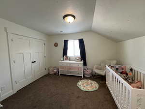 Bedroom featuring a textured ceiling, visible vents, a nursery area, lofted ceiling, and dark carpet